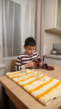 Oğlan bardakları ve bardakları havluyla siler. Ev işleri..