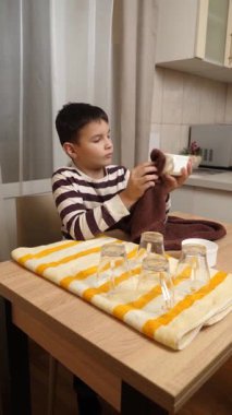 Oğlan bardakları ve bardakları havluyla siler. Ev işleri..