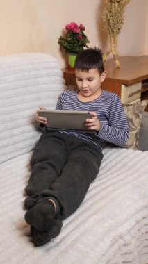 Bir çocuk kanepede otururken tablette oyun oynuyor..