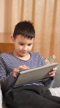 Bir çocuk kanepede otururken tablette oyun oynuyor..