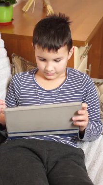 Bir çocuk kanepede otururken tablette oyun oynuyor..