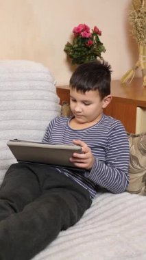 Bir çocuk kanepede otururken tablette oyun oynuyor..