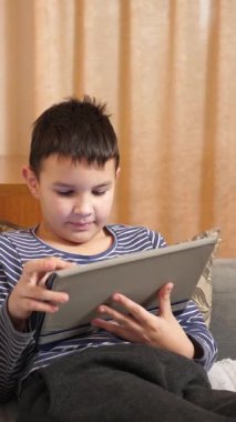 Bir çocuk kanepede otururken tablette oyun oynuyor..