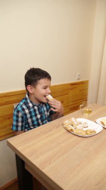 Bir çocuk masada otururken kurabiye yer ve çay içer..