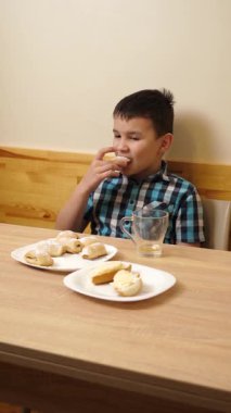Bir çocuk masada otururken kurabiye yer ve çay içer..