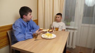 Çocuklar masada otururken sandviç, meyve yiyip çay içiyorlar.