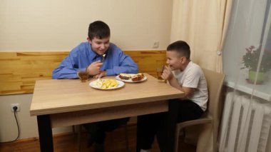 Çocuklar masada otururken sandviç, meyve yiyip çay içiyorlar.