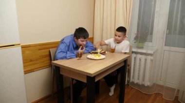 Çocuklar masada otururken sandviç, meyve yiyip çay içiyorlar.