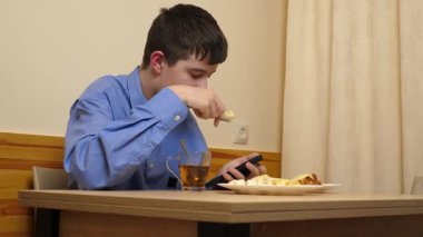 Ergen sandviç yiyor ve masada otururken çay içiyor.