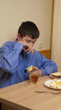 Ergen sandviç yiyor ve masada otururken çay içiyor.