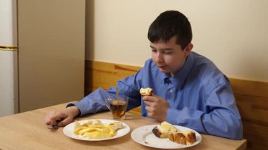 Ergen sandviç yiyor ve masada otururken çay içiyor.