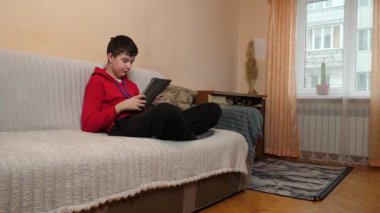 Bir genç kanepede otururken tablet kullanır..