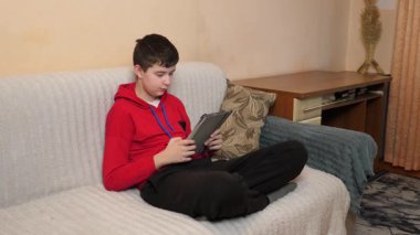 Bir genç kanepede otururken tablet kullanır..