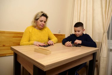 Anne ve oğlu masada domino oynuyorlar. Ev eğlencesi.