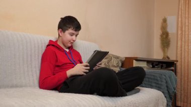 Bir genç kanepede otururken tablet kullanır..