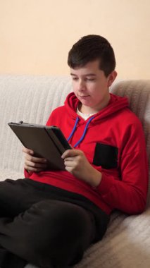 Bir genç kanepede otururken tablet kullanır..