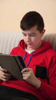 Bir genç kanepede otururken tablet kullanır..