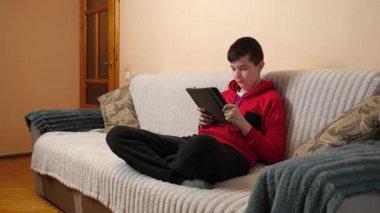 Bir genç kanepede otururken tablet kullanır..