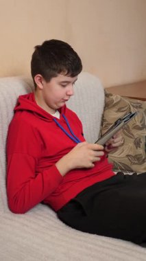 Bir genç kanepede otururken tablet kullanır..