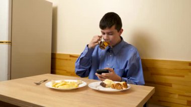 Ergen sandviç yiyor ve masada otururken çay içiyor.