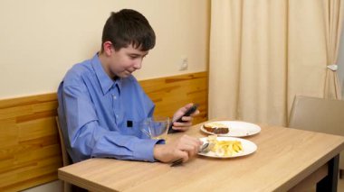 Ergen sandviç yiyor ve masada otururken çay içiyor.