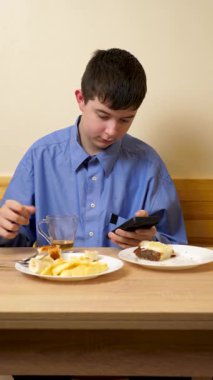 Ergen sandviç yiyor ve masada otururken çay içiyor.