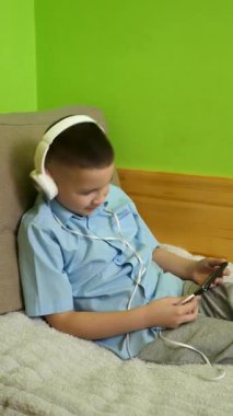 Bir çocuk kulaklıklı bir akıllı telefondan müzik dinlemekten hoşlanır..