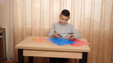 Çocuk renkli kartondan bir zanaat yapıyor, hatları işaretliyor..