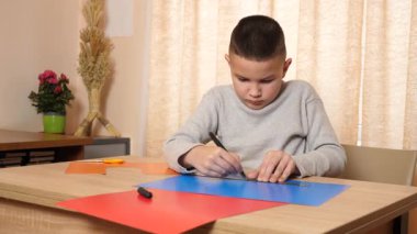 Çocuk renkli kartondan bir zanaat yapıyor, hatları işaretliyor..