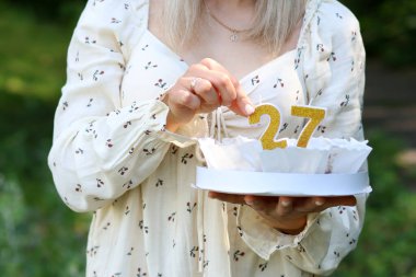 Kadın bir pastanın içine 27 numara şeklinde bir mum koyar. Doğum günü kutlaması.