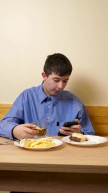 Ergen sandviç yiyor ve masada otururken çay içiyor.