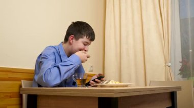 Ergen sandviç yiyor ve masada otururken çay içiyor.