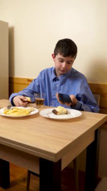 Ergen sandviç yiyor ve masada otururken çay içiyor.