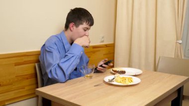 Ergen sandviç yiyor ve masada otururken çay içiyor.