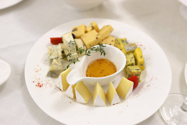 A gourmet cheese platter with assorted cheeses, fresh strawberries, herbs, and honey mustard dip on a white plate, perfect for an elegant appetizer or wine pairing