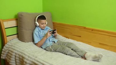Bir çocuk kulaklıklı bir akıllı telefondan müzik dinlemekten hoşlanır..