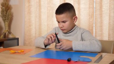 Çocuk renkli kartondan bir zanaat yapıyor, hatları işaretliyor..
