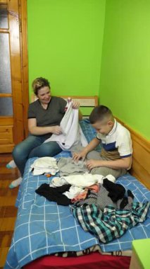 Oğlan annesinin elbiselerini katlamasına yardım eder. Ev işleri..