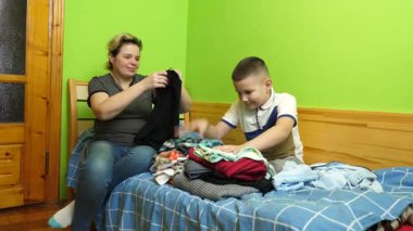 Oğlan annesinin elbiselerini katlamasına yardım eder. Ev işleri..