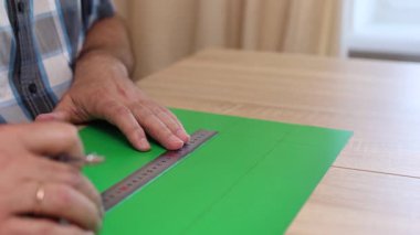 Renkli karton üzerine kesme çizgileri çizen eller, kağıt modeli için el yapımı şablon, DIY proje hazırlığı.