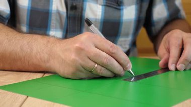 Renkli karton üzerine kesme çizgileri çizen eller, kağıt modeli için el yapımı şablon, DIY proje hazırlığı.