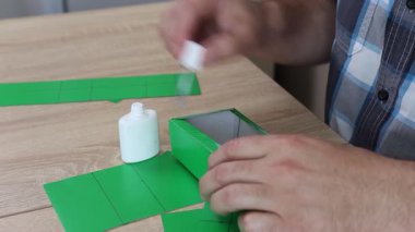 Eller karton kesikleri katlıyor ve yapıştırıyor, yaratıcı DIY zanaat projesi için kağıt modelinin parçalarını birleştiriyor.