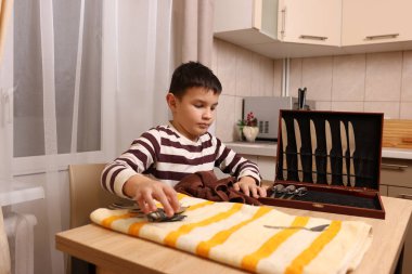 Oğlan çatal ve mutfak bıçaklarını siliyor. Ev işleri..