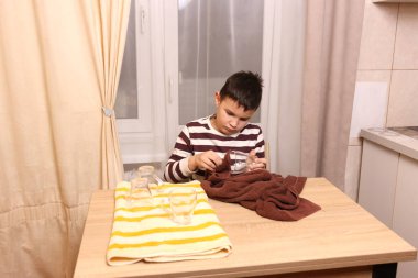 Oğlan bardakları ve bardakları havluyla siler. Ev işleri..