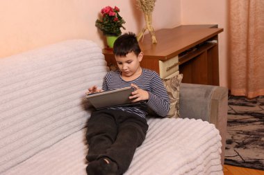 Bir çocuk kanepede otururken tablette oyun oynuyor..