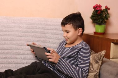 Bir çocuk kanepede otururken tablette oyun oynuyor..