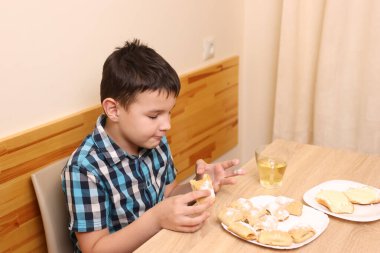 Bir çocuk masada otururken tatlı çörekler yer ve çay içer..
