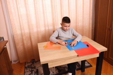 Bir çocuk masada otururken renkli kağıtlardan başvuru yapıyor. Yaratıcılık ve eğlence kavramı.