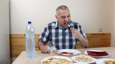 Adam mutfak masasında otururken su içip yemek yiyor.