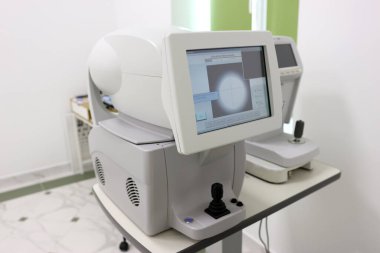 Kırılma hatalarını doğru bir şekilde tespit etmek için otomatik göz ölçümlerinde kullanılan, beyaz klinik bir ortamda monitör, klavye ve fare ile modern otomatik otomatik fraktör..